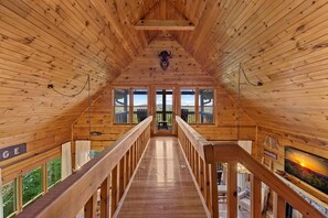 Ein Holzinnenraum mit hoher Decke, einer zentralen Treppe und großen Fenstern mit Blick ins Freie.