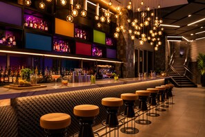 Un espace bar doté d’un long comptoir, de tabourets, de luminaires sphériques suspendus et d’étagères remplies de bouteilles.