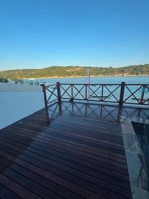 A wooden deck with a railing overlooking a body of water and a hilly landscape. - Not That Ugly Villa Cantik (Klungkung)