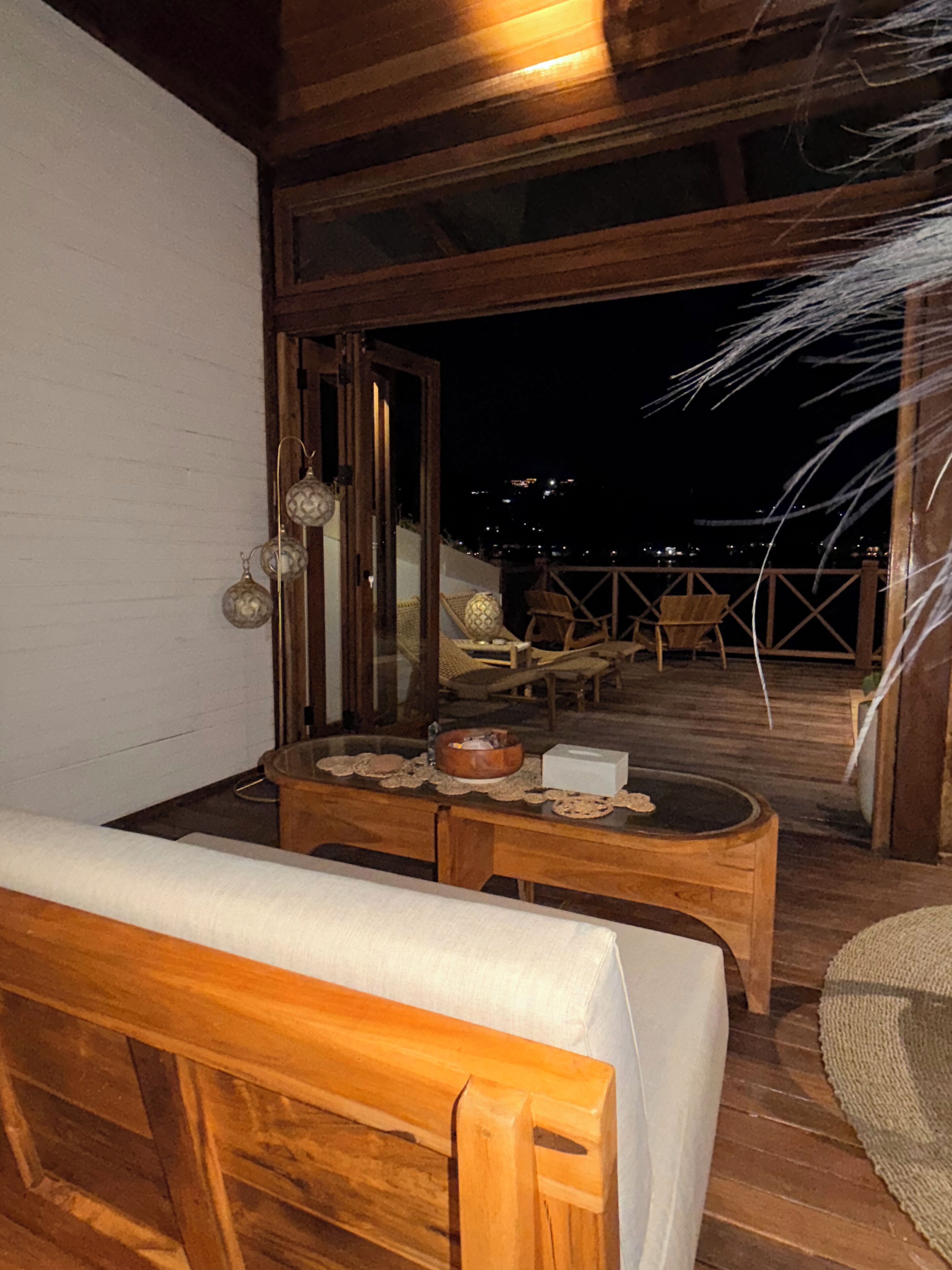 Uma área de estar ao ar livre com mobiliário de madeira e vista para a cidade à noite.