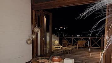 Uma área de estar ao ar livre com mobiliário de madeira e vista para a cidade à noite.