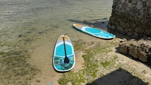 Dos tablas de remo en una playa arenosa cerca de un muro de piedra.