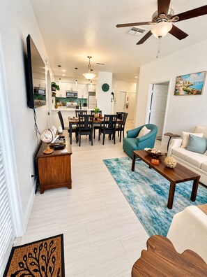 A modern living room with a dining area, a ceiling fan, and a kitchen in the background. - Resort-style Condo Near Disney 3BR/2BR Sleeps 6 (Kissimmee)