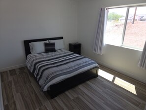 A bedroom with a bed, a nightstand, a window with curtains, and a view of the outside.