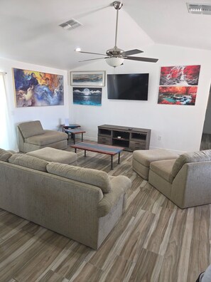 A living room with a ceiling fan, a flat-screen TV, and artwork on the walls.