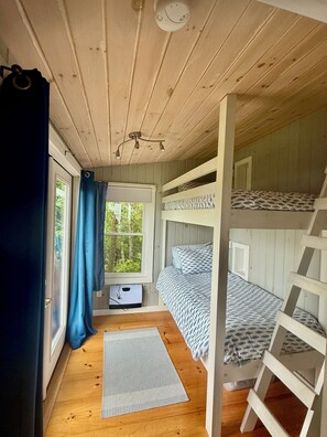 A cabin with a bunk bed, a window with curtains, a ceiling light, and a small window with a thermostat.