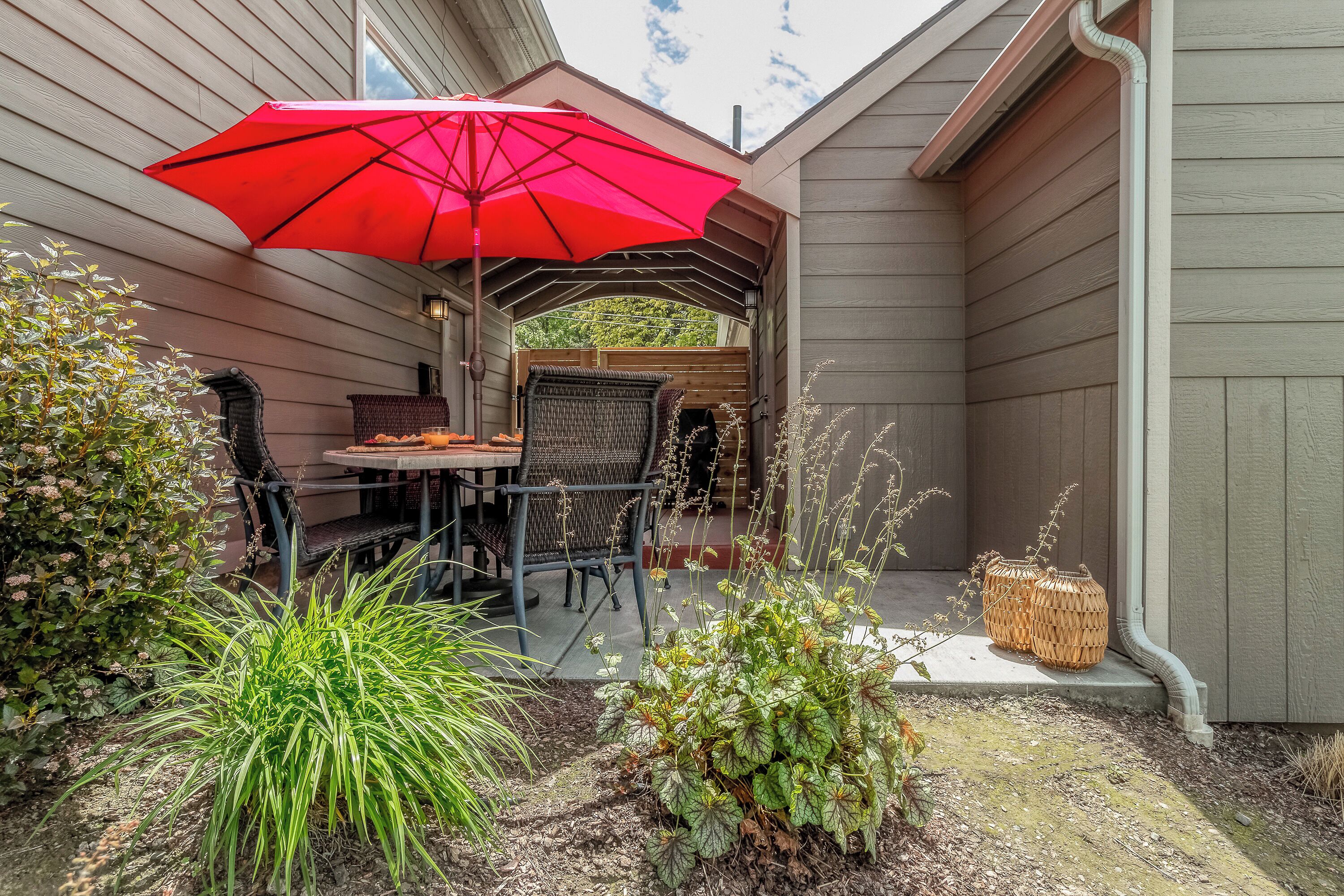 Une terrasse couverte avec une table et des chaises, un parasol rouge et diverses plantes.