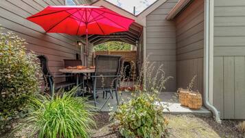 Une terrasse couverte avec une table et des chaises, un parasol rouge et diverses plantes.