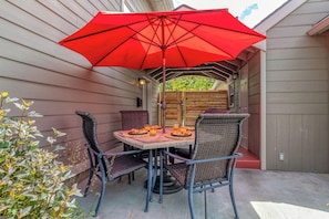 Une terrasse avec une table et des chaises sous un parasol rouge, entourée de plantes.