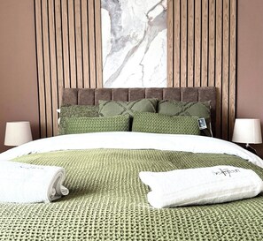 A hotel room with a bed, pillows, a headboard, and a wall-mounted artwork.