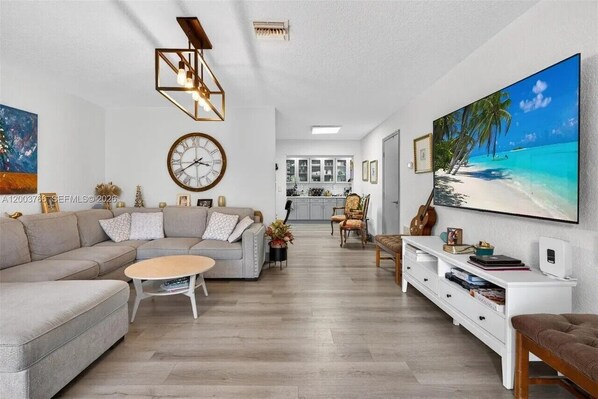 Ein modernes Wohnzimmer mit einer Couch, einem Couchtisch und einem Fernseher, der eine Strandansicht zeigt.