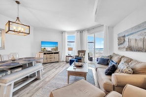 A spacious living area with a dining table, sofa, and a large window with a view. - Dunes of Seagrove 302B - Gulf front with great views! (Santa Rosa Beach)
