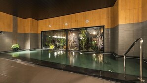 Una piscina con pared de vidrio, paneles de madera y barandilla metálica.