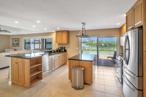 A modern kitchen with a large island, stainless steel appliances, and a view of a lake. - Coastal Osprey Retreat with Dock, Pool & Water Views (Osprey)