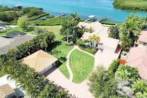 A residential area with houses, a well-maintained lawn, and a body of water in the background. - Coastal Osprey Retreat with Dock, Pool & Water Views (Osprey)