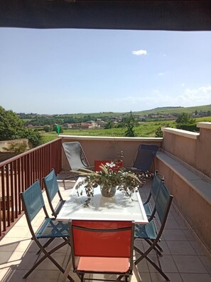 A terrace with a table and chairs, a potted plant, and a view of a green landscape. - Le Camelia - CHENAS - Gîte (CHENAS)