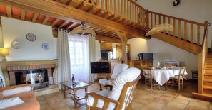 A cozy living room with a fireplace, wooden furniture, and a staircase. - Le Camelia - CHENAS - Gîte (CHENAS)