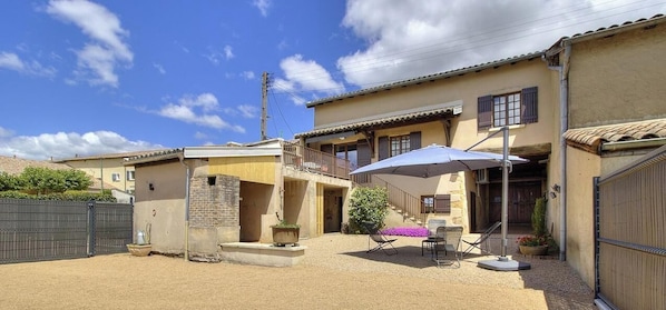A two-story building with a balcony, outdoor seating, and a gravel courtyard.