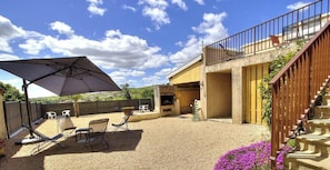 A patio with outdoor furniture, a barbecue grill, and a staircase leading to a balcony.