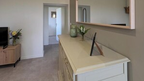 A modern living room with a television, a wooden cabinet, a beige dresser, a large mirror, and a vase with flowers. - Bird Paradise (POMMIERS)