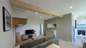 A modern living room with a television, sofa, and a dining area with a table and chairs. - Bird Paradise (POMMIERS)