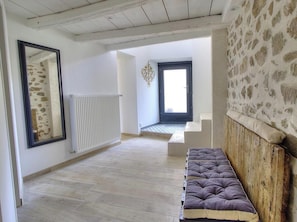 A room with a wooden bench, a radiator, a stone wall, and a door leading to a balcony.