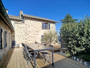 A stone building with a wooden deck, outdoor seating, and a tree.