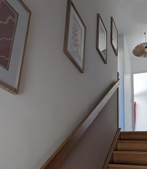 Eine Treppe mit Holzstufen und einer Handlauf, die zu einem Raum mit weißer Wand und gerahmten Kunstwerken führt.
