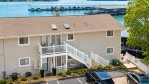A two-story building with a balcony, parking lot, and a view of a lake with docks. - Serenity Oasis - Close to all the fun (Osage Beach)
