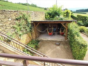 A stone wall, a wooden pergola with hanging hammocks, and a staircase leading to an upper level. - Gîte de Pelozane - CHARNAY (CHARNAY)