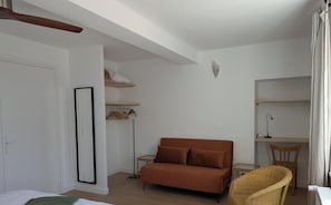 Une piÚce comprenant un lit, un canapé marron, un bureau avec une chaise, un lampadaire et un fauteuil en osier.