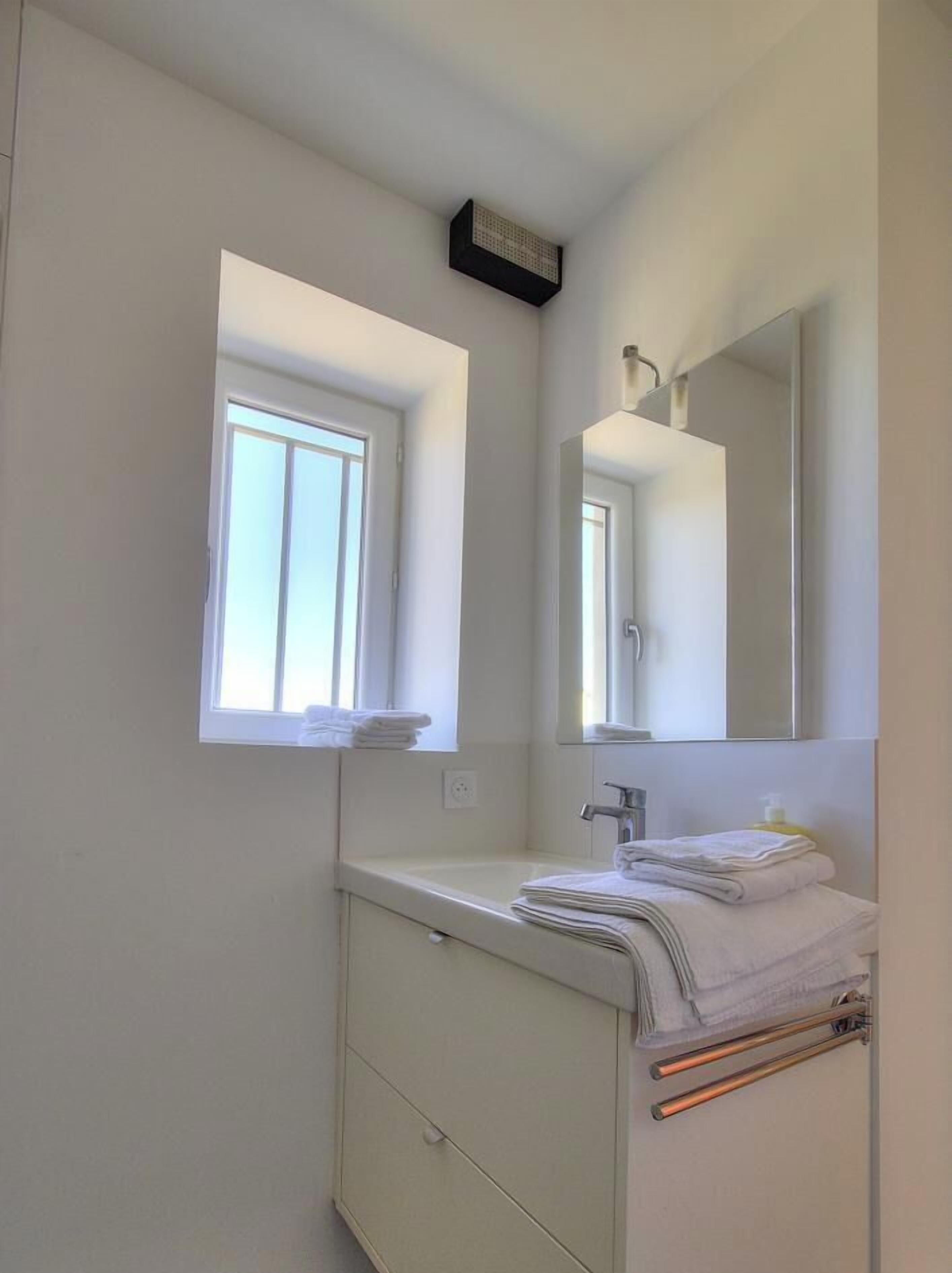 A bathroom with a window, a mirror, a sink, and a towel rack.