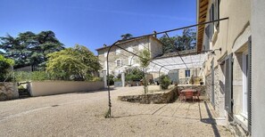 A courtyard with a stone wall, a metal pergola, and a building with a tiled roof.