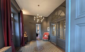 A hallway with patterned flooring, a chandelier, a red chair, and a door with glass panels.
