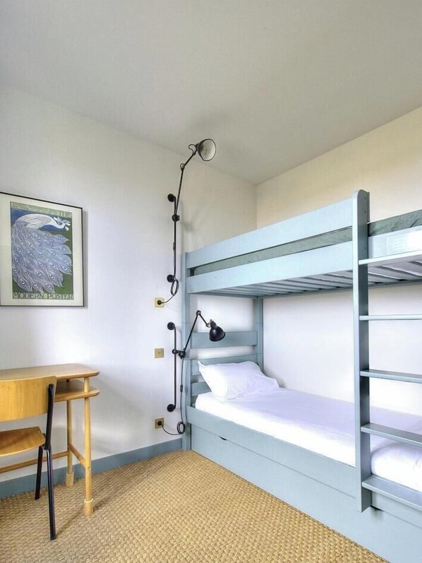 Ein Etagenbett mit Schreibtisch und Lampe, ein gerahmtes Poster an der Wand und eine gewebte Fußmatte.