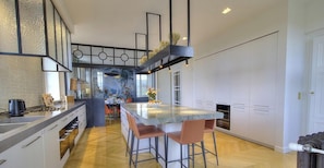 A modern kitchen with a central island, bar stools, and a view into the dining area.