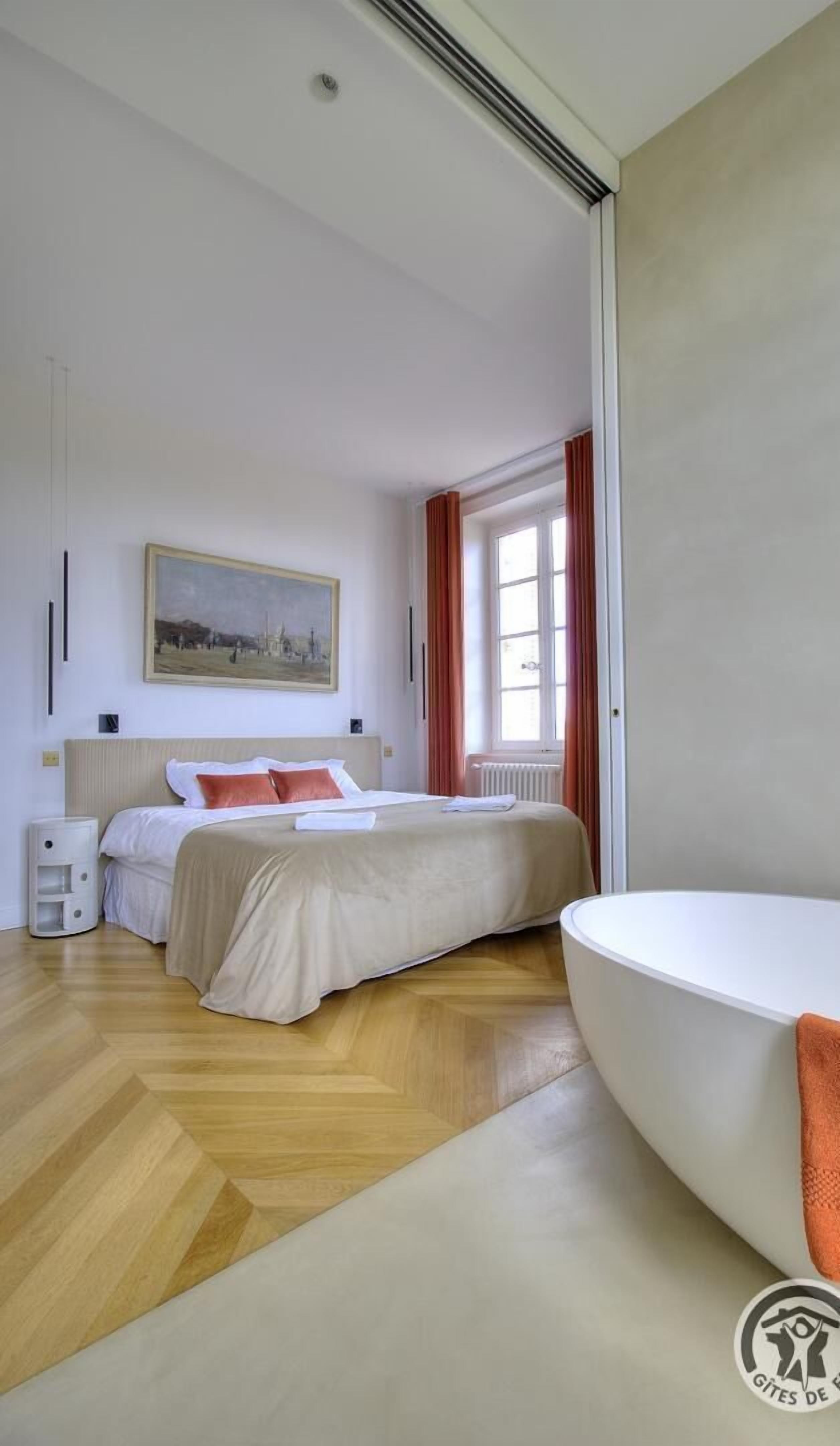 Ein Hotelzimmer mit einem Bett, einem Gemälde, einem Fenster mit Vorhängen, einem Heizkörper und einer weißen Badewanne.