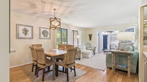 A dining area with a wooden table and wicker chairs, a chandelier, and framed artwork on the walls.