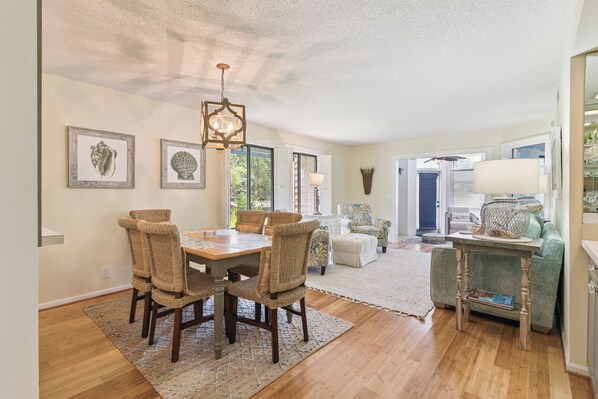 A dining area with a wooden table and wicker chairs, a chandelier, and framed artwork on the walls.