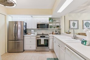 A modern kitchen with stainless steel appliances, white cabinetry, and a herringbone-patterned backsplash.