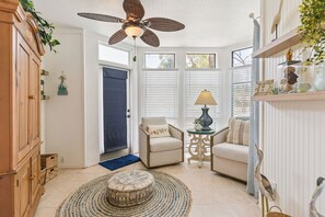 Una habitación con ventilador de techo, sofá, sillón, lámpara y una estatua decorativa de un pájaro.
