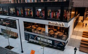 Ein modernes Gebäude mit einem 'Puttshack'-Schild, Außenbestuhlung und einer 'The Interlock'-Werbeanzeige.