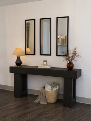 Ein dunkles Holzkonsole mit drei Spiegeln, einer Lampe und einer Vase mit getrockneten Blumen.