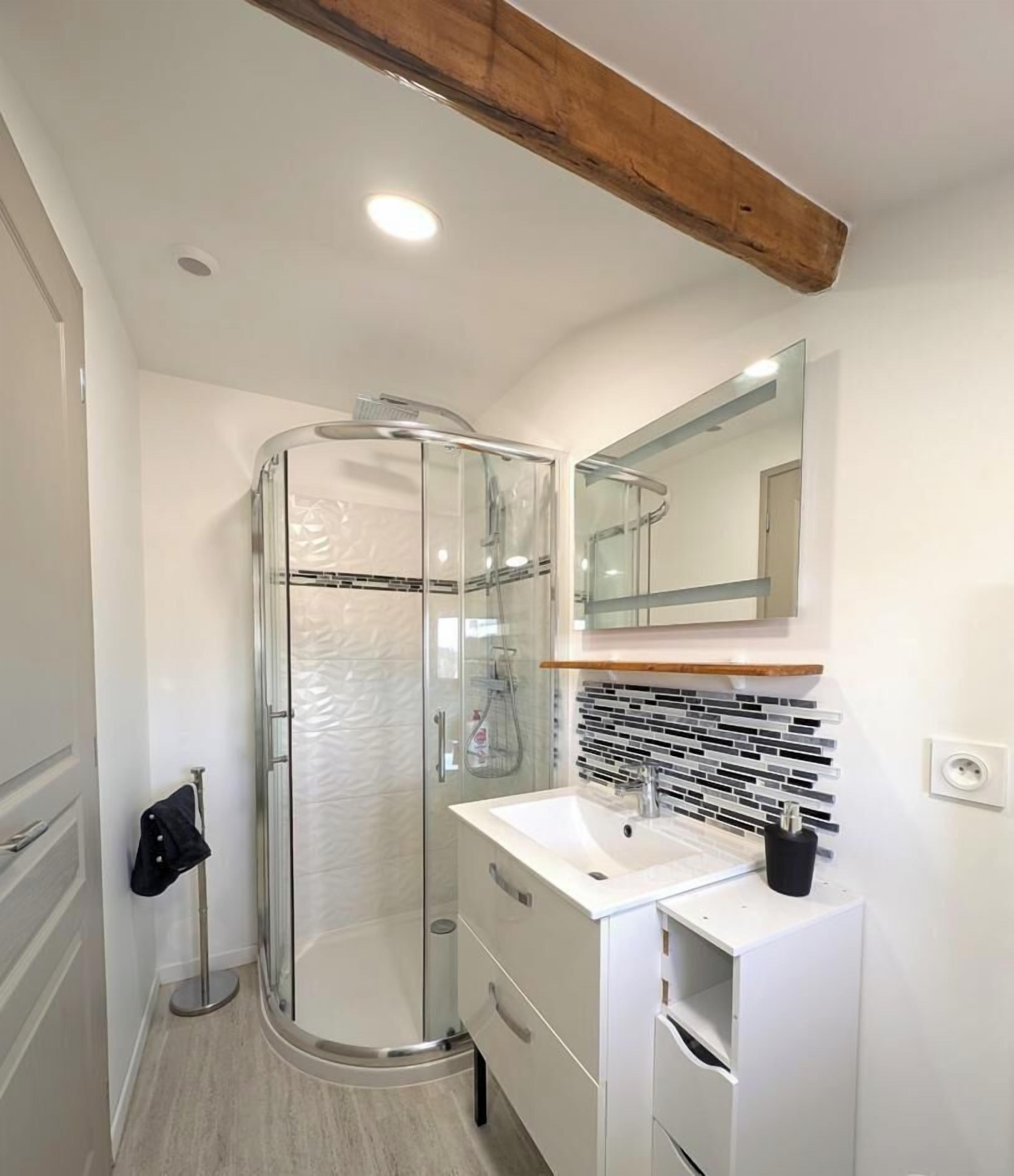 Un bagno moderno con cabina doccia in vetro, lavandino bianco e specchio sopra il mobile.