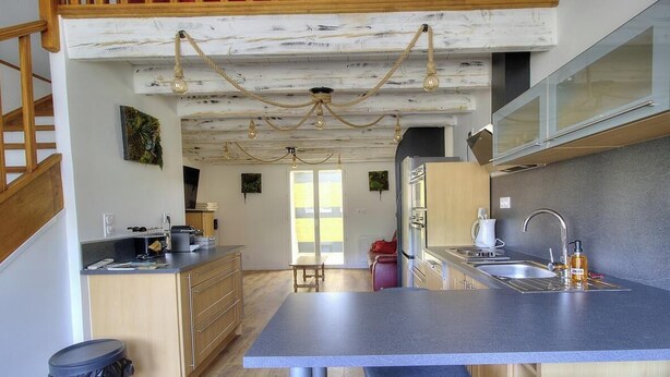 A modern kitchen with a central island, wooden cabinets, and a staircase. - Gîte de Timbout - LES HAIES (LES HAIES)