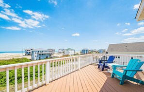 A wooden deck with a railing, blue Adirondack chairs, and a view of the beach and ocean. - Ocean Aire - 4x4 Carova Beach, Ocean View, Hot Tub, Large Decks, Pets OK, Kayaks (Carova Beach)