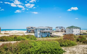 A beachfront property with multiple houses, a sandy beach, and a clear blue sky. - Ocean Aire - 4x4 Carova Beach, Ocean View, Hot Tub, Large Decks, Pets OK, Kayaks (Carova Beach)