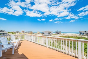 A wooden deck with white chairs, a white railing, and beach houses in the background. - Ocean Aire - 4x4 Carova Beach, Ocean View, Hot Tub, Large Decks, Pets OK, Kayaks (Carova Beach)