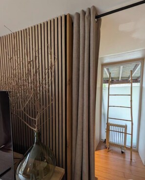 Ein Zimmer mit einer Wand aus Holzlatten, einer Glasvase mit Zweigen, einer Holzleiter und Blick auf einen Balkon.