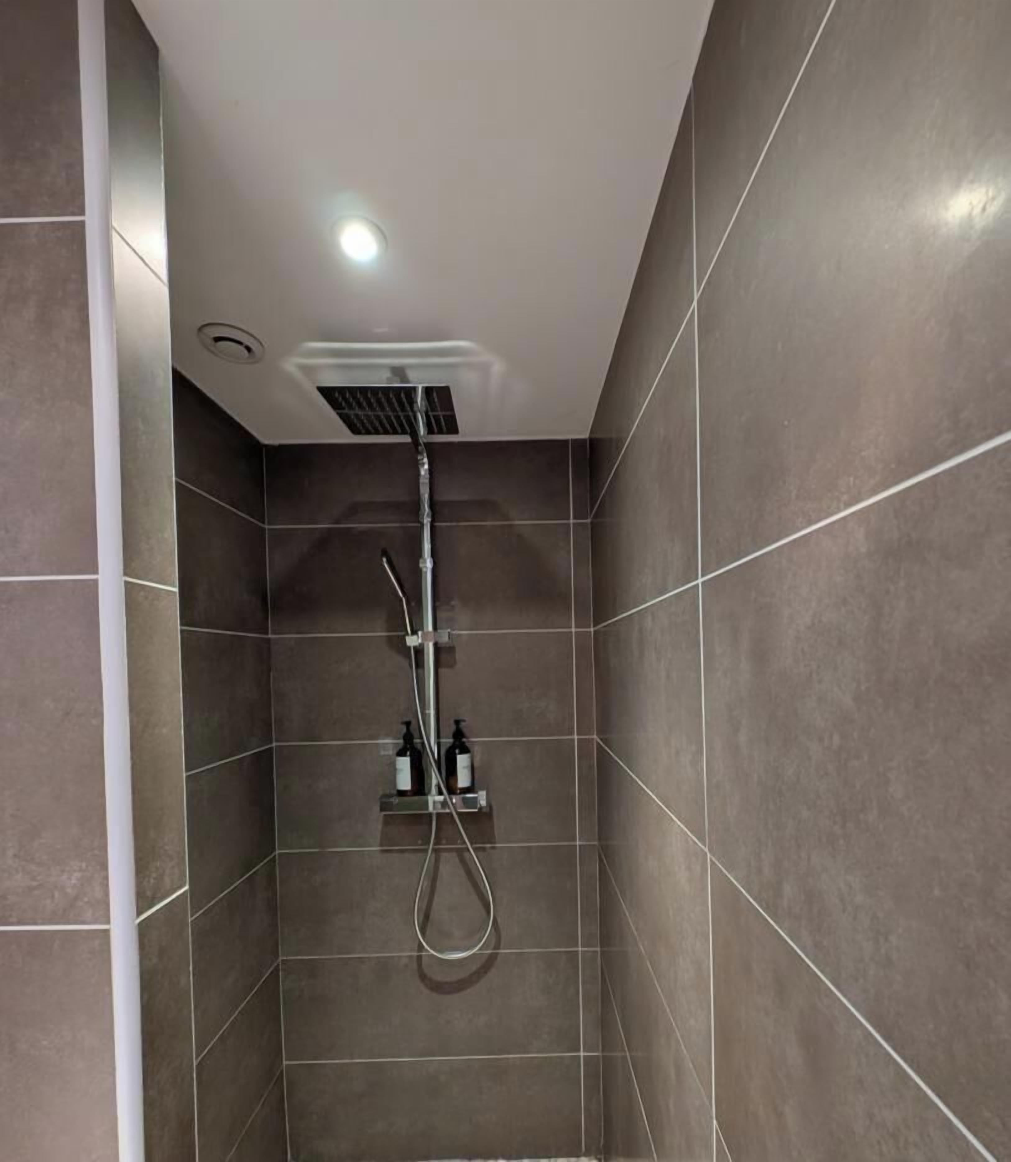 A modern shower with a handheld showerhead and a wall-mounted control panel.